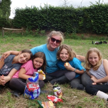 A young lady with her arms around four girls, all smiling enjoying their picnic